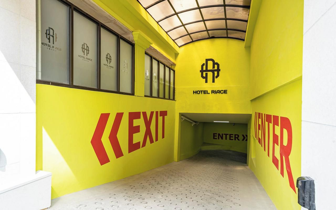 Ein Hotelkorridor mit Schildern für AUSGANG und EINTRITT, einer Decke mit Gittermuster und dem Logo von HOTEL RIACE.