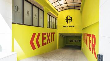 Ein Hotelkorridor mit Schildern für AUSGANG und EINTRITT, einer Decke mit Gittermuster und dem Logo von HOTEL RIACE.
