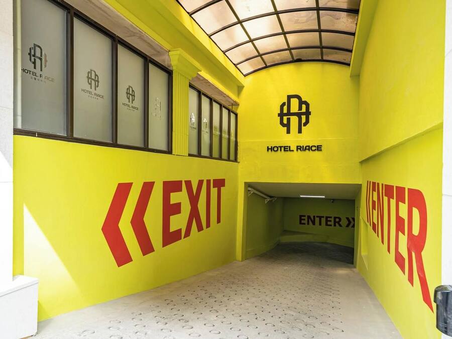 Ein Hotelkorridor mit Schildern für AUSGANG und EINTRITT, einer Decke mit Gittermuster und dem Logo von HOTEL RIACE.