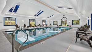 En stor indendørs swimmingpool med krystalklart vand, omgivet af liggestole og et højt loft med ovenlys.