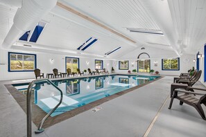 A large indoor swimming pool with a clear blue water surface, surrounded by lounge chairs and a high ceiling with skylights. - White Loop Condo 2 Bedroom Condo (Ludlow)
