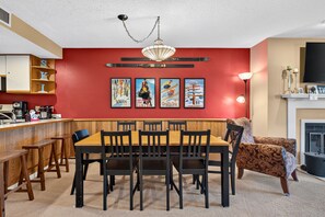 A dining area with a wooden table and chairs, a red accent wall, and framed vintage posters. - White Loop Condo 2 Bedroom Condo (Ludlow)