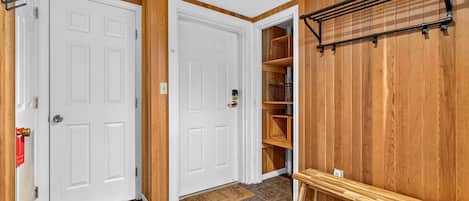 A hallway with two white doors, a wooden bench, a shelf with baskets, and a wall-mounted rack.