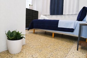 Een slaapkamer met een bed, een nachtkastje, een kamerplant, een donkere dressoir en een raam met gordijnen.