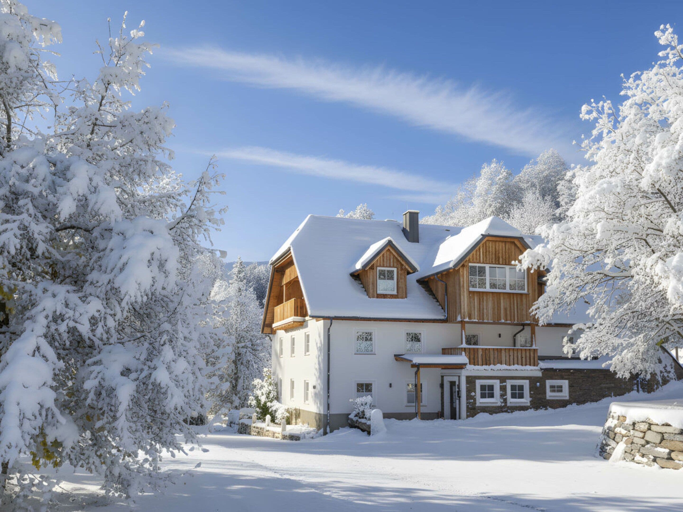 Una casa de madera de dos pisos con un techo cubierto de nieve, rodeada de árboles cargados de nieve.