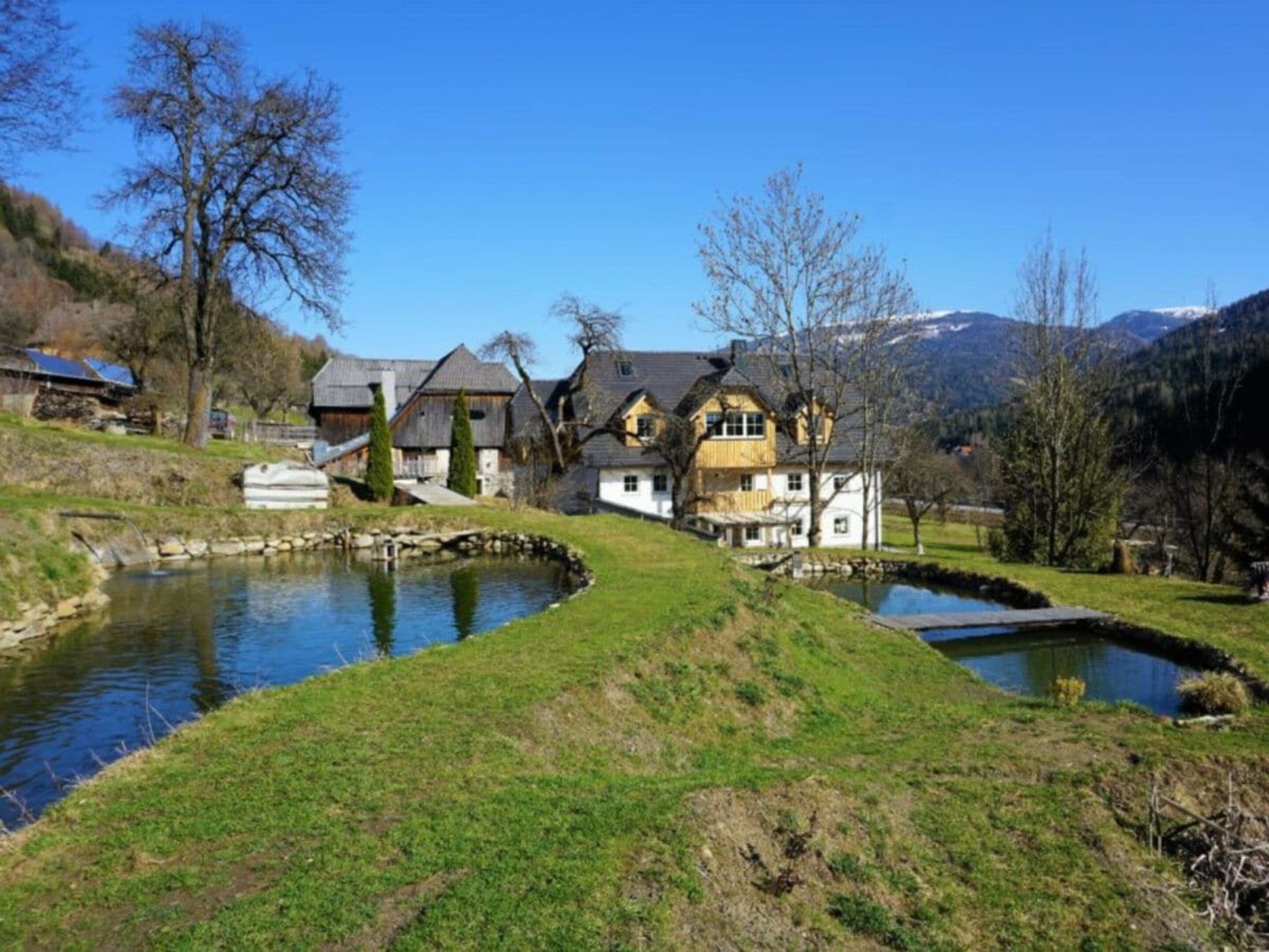 Una grande casa con diversi edifici, uno stagno e un paesaggio collinare.
