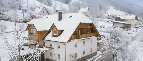 Una casa de dos pisos con techo inclinado, fachada de madera y un paisaje cubierto de nieve.