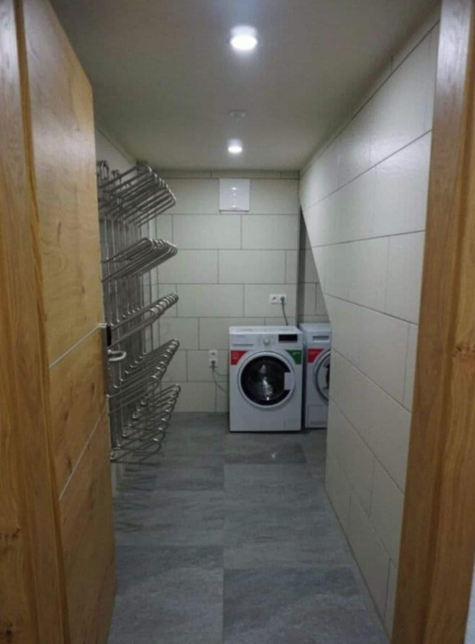 Corredor estreito com uma estante de metal à esquerda e uma máquina de lavar à direita.
