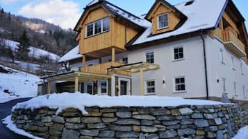 Ein zweistöckiges Holzhaus mit einer Mauer aus Stein davor, umgeben von Schnee.