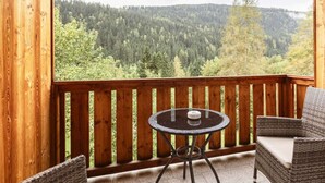 A wooden balcony with a round table and two wicker chairs, overlooking a forested valley. - Apartment With 1 Bedroom (Sankt Georgen am Kreischberg)