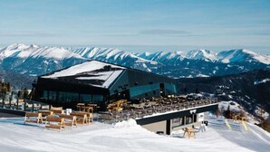 A modern building with a ski lift and snow-covered mountains in the background. - Apartment With 1 Bedroom (Sankt Georgen am Kreischberg)