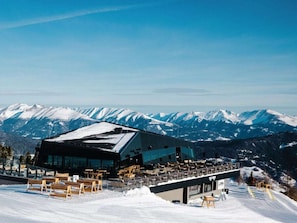 En moderne bygning med en skilift og snedækkede bjerge i baggrunden.