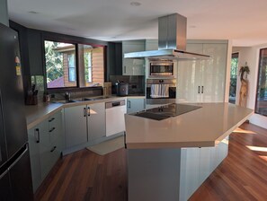 A modern kitchen with a central island, built-in appliances, and a view of the outdoors. - Luxury 5 bed home, spa, games room, pool, slide, firepit, nearby hikes, (Samford Valley)