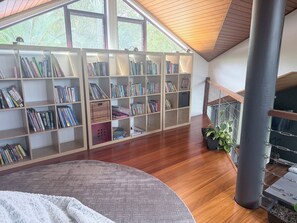 A spacious room with a large skylight, wooden flooring, and a built-in bookshelf filled with books. - Luxury 5 bed home, spa, games room, pool, slide, firepit, nearby hikes, (Samford Valley)