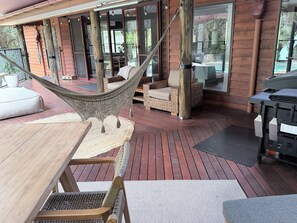 A wooden deck with outdoor furniture, including a hammock, wicker chairs, and a table. - Luxury 5 bed home, spa, games room, pool, slide, firepit, nearby hikes, (Samford Valley)