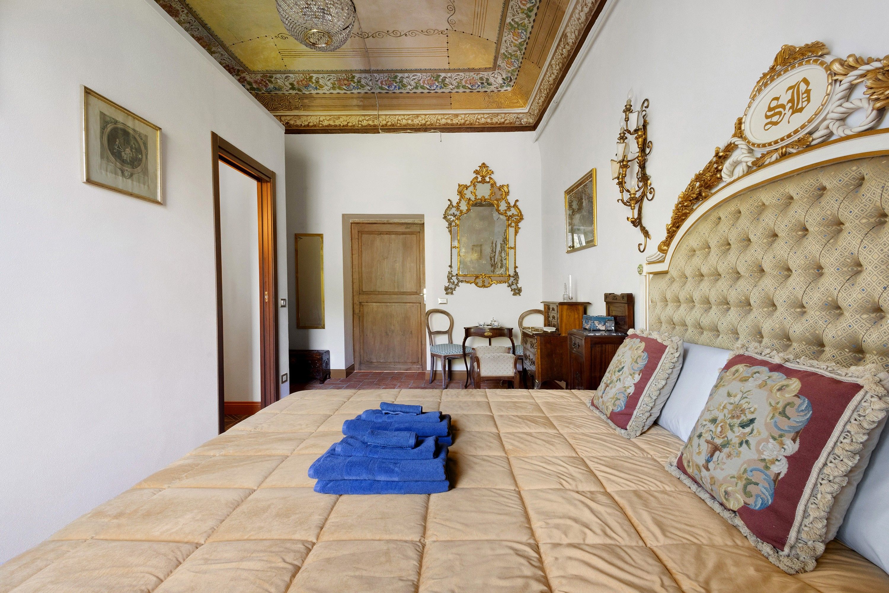 Una camera d'albergo con un letto grande, un lampadario, decorazioni elaborate alle pareti e una porta in legno.