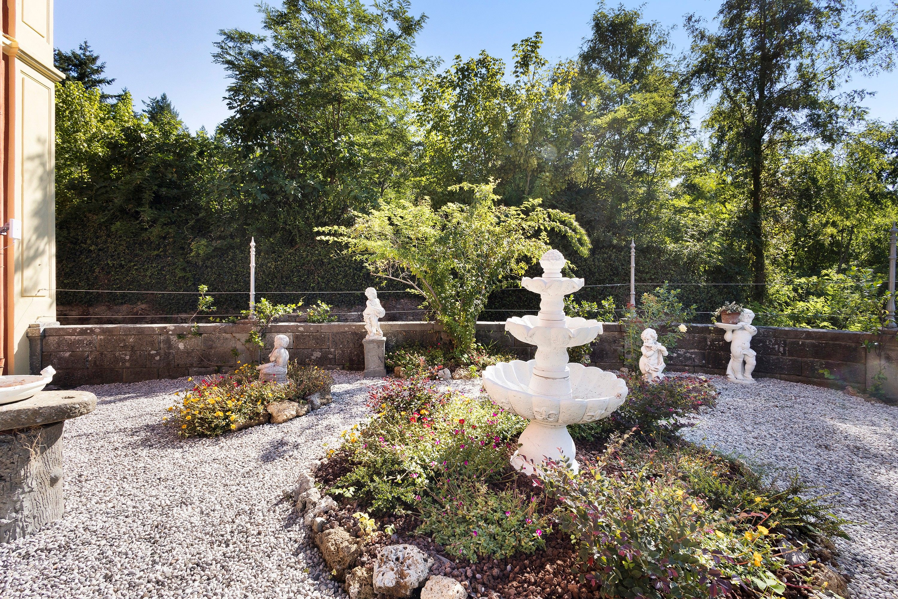 A garden with a central fountain, surrounded by gravel and various plants.