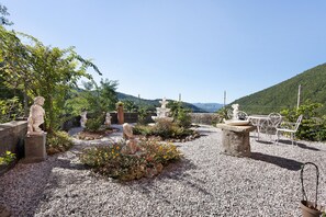 Ein Garten mit Statuen, einer Bank und Blick auf einen Berg.