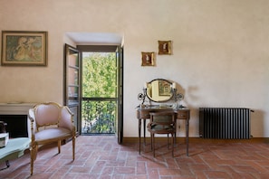 Une pièce comprenant une chaise, une commode avec un miroir, un radiateur et une fenêtre donnant sur un espace verdoyant.