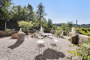 Une terrasse extérieure avec une table et des chaises, entourée de murs en pierre et de verdure.