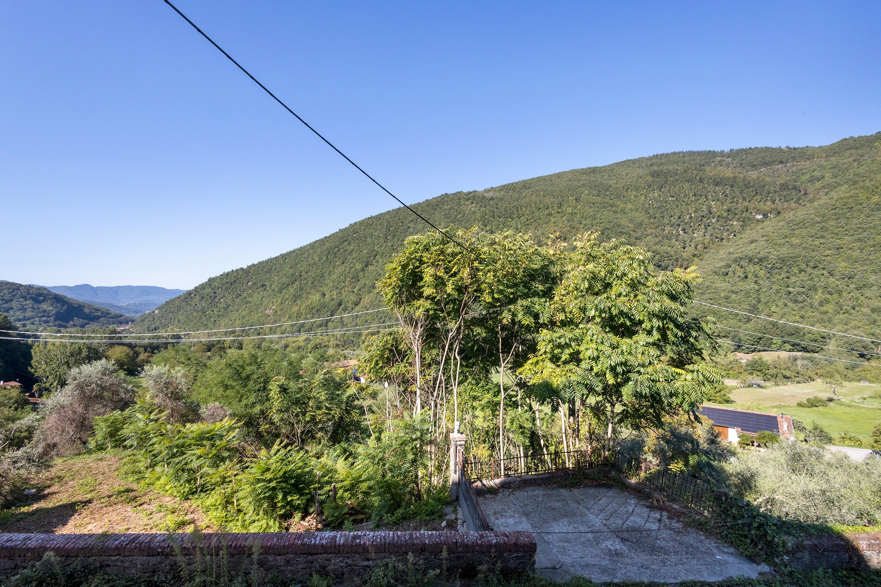 Paesaggio rurale con una collina, alberi e una costruzione in mattoni.