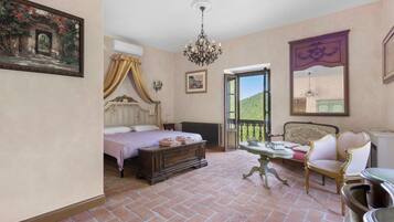Una camera da letto con un letto, una cassettiera, un tavolo e una sedia. Una finestra offre vista su un paesaggio verde.