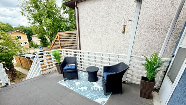 An outdoor patio area with a white fence, two wicker chairs, a small round table, and a patterned rug. - Your private terrace next to St Boniface Université and Hospital Ver Walkable (Winnipeg)