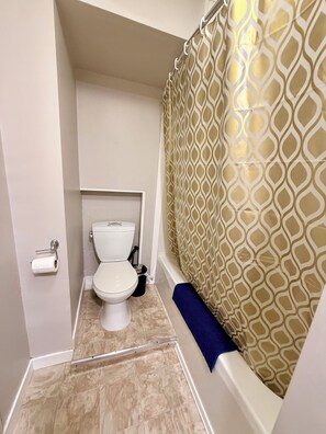 Een badkamer met toilet, een douchegordijn met geometrisch patroon en een blauwe handdoek.