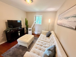 Een woonkamer met een flatscreen televisie, een bank, een bijzettafeltje, een kamerplant en een schilderij aan de muur.