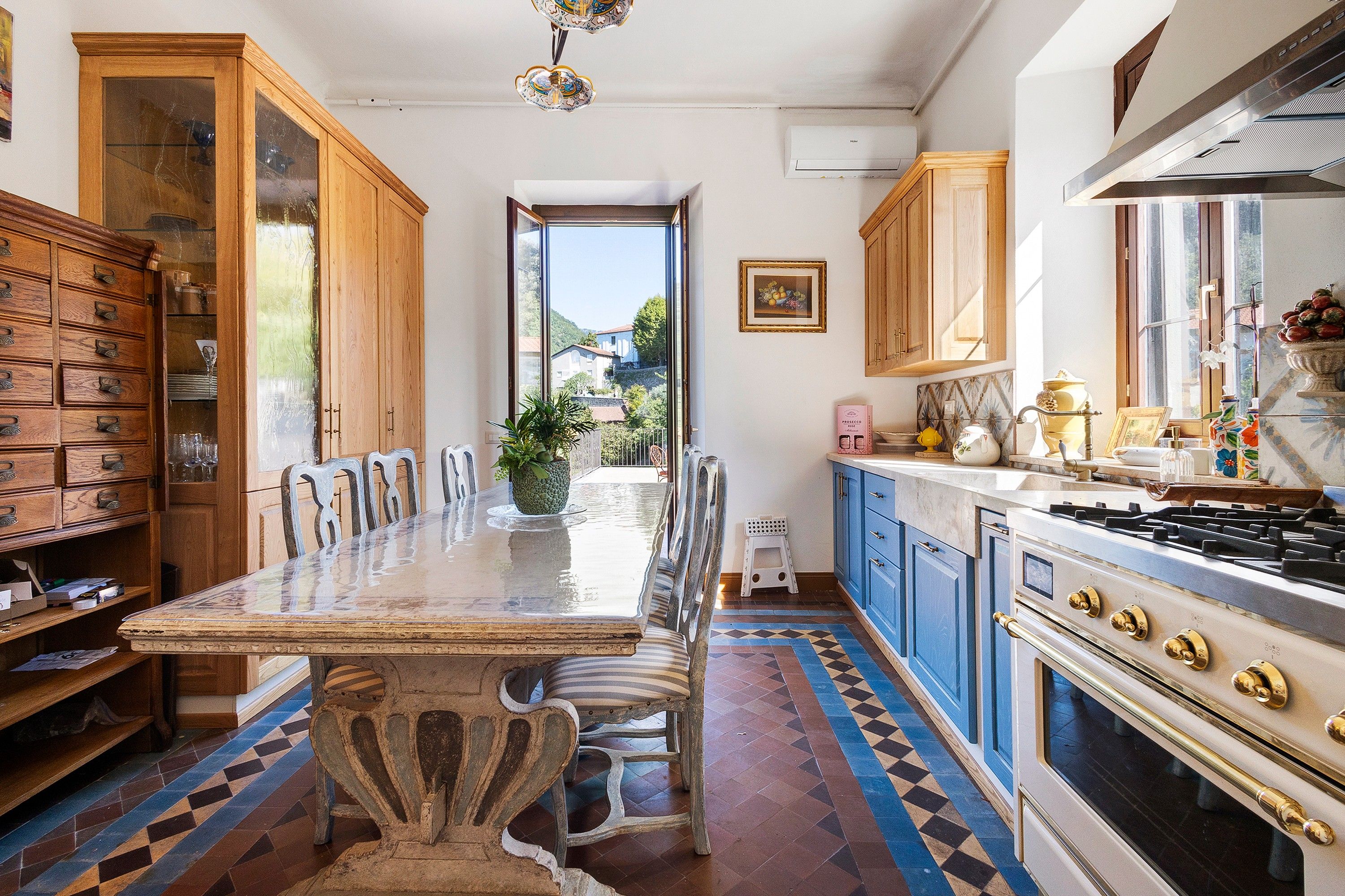 A kitchen with a long dining table, wooden cabinets, and a view to the outside.