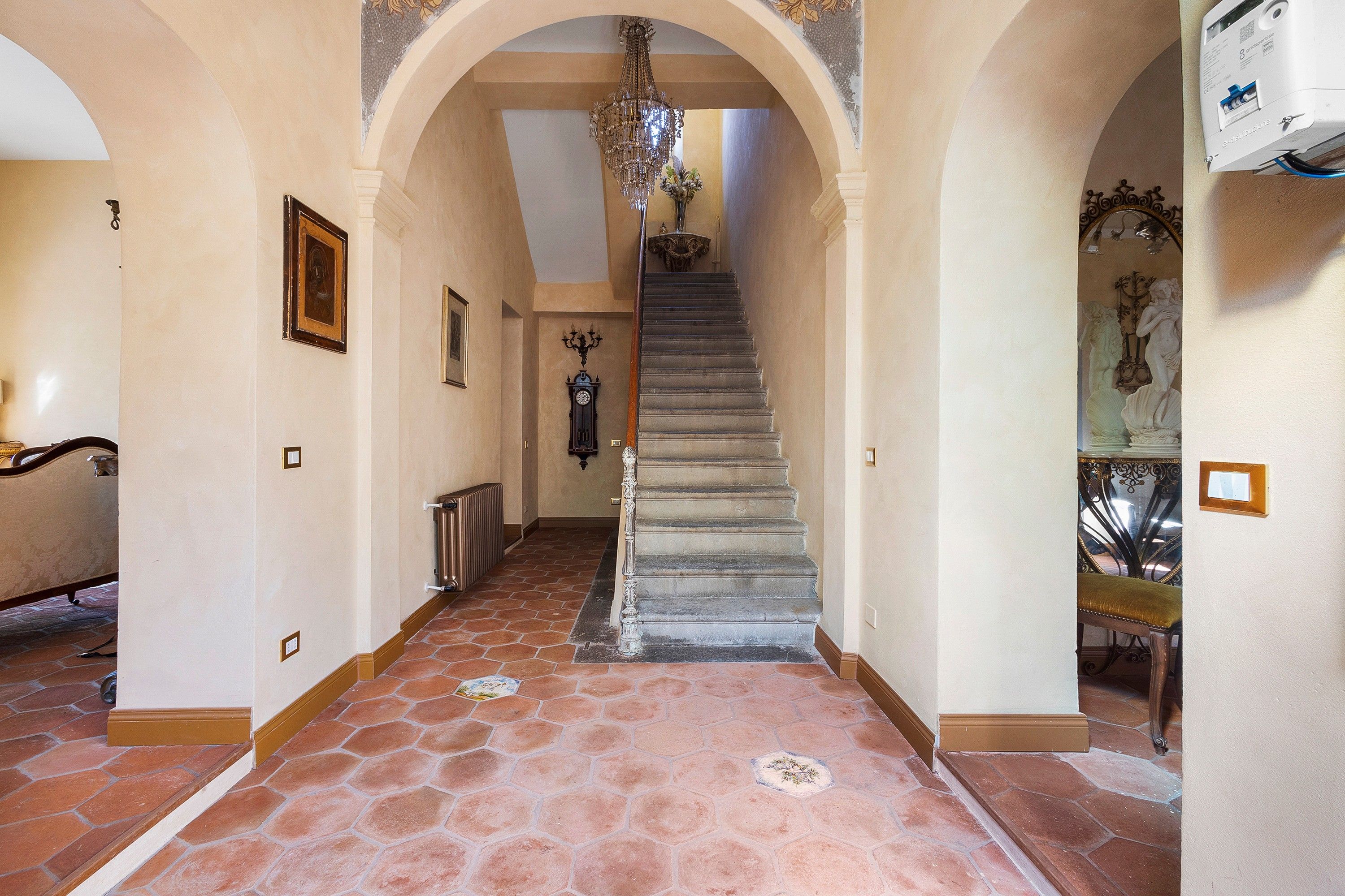 A grand hallway with a staircase, ornate wall decorations, and a chandelier.