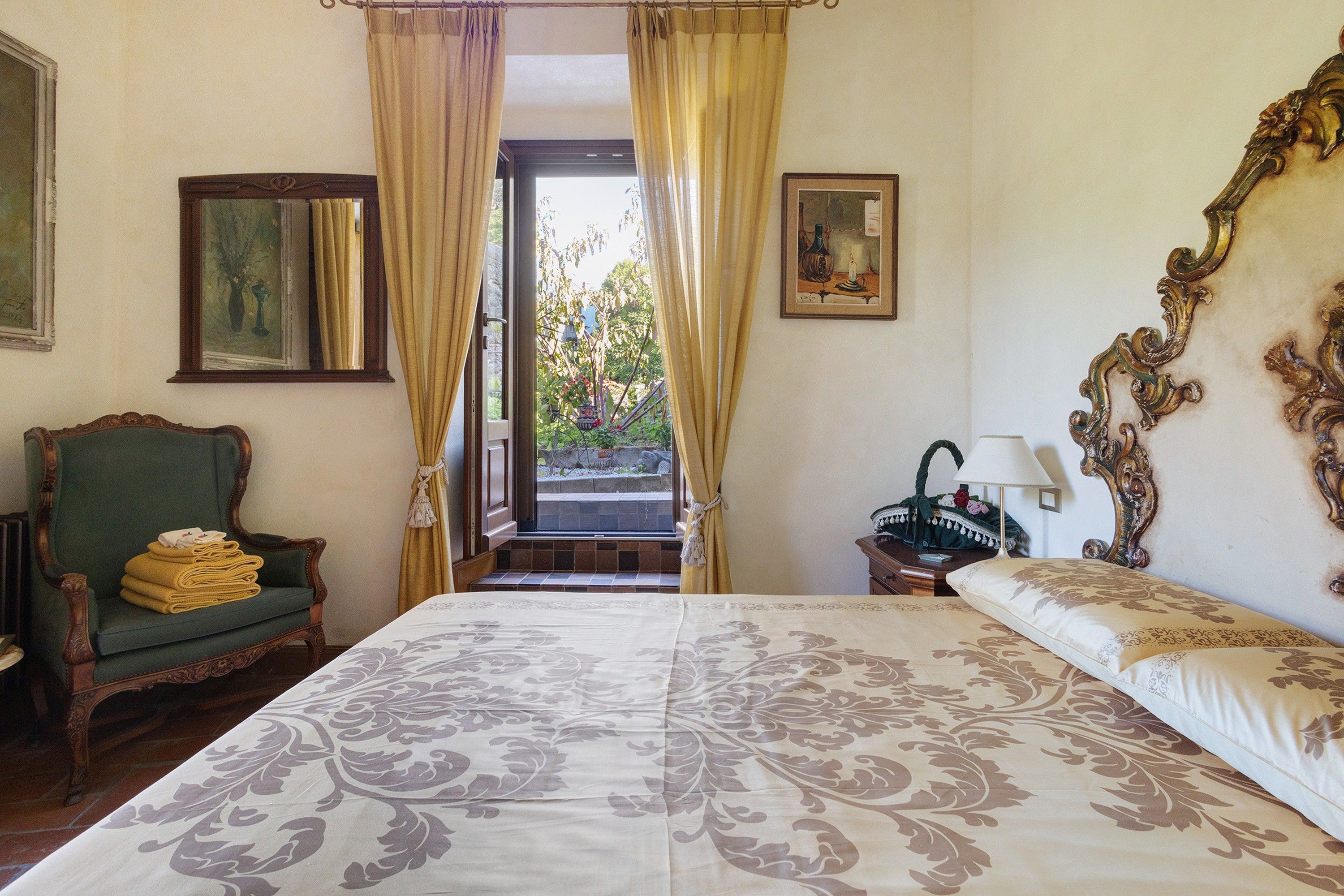 Una camera da letto con un letto grande, una sedia con un asciugamano piegato, un comodino con una lampada e vista all'esterno tramite una finestra.
