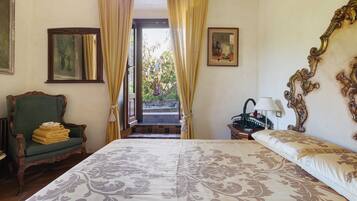 Una camera da letto con un letto grande, una sedia con un asciugamano piegato, un comodino con una lampada e vista all'esterno tramite una finestra.