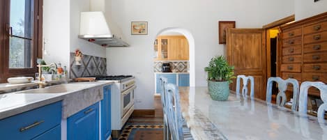 Uma cozinha com armários azuis, bancada de mármore e uma ilha central com cadeiras.