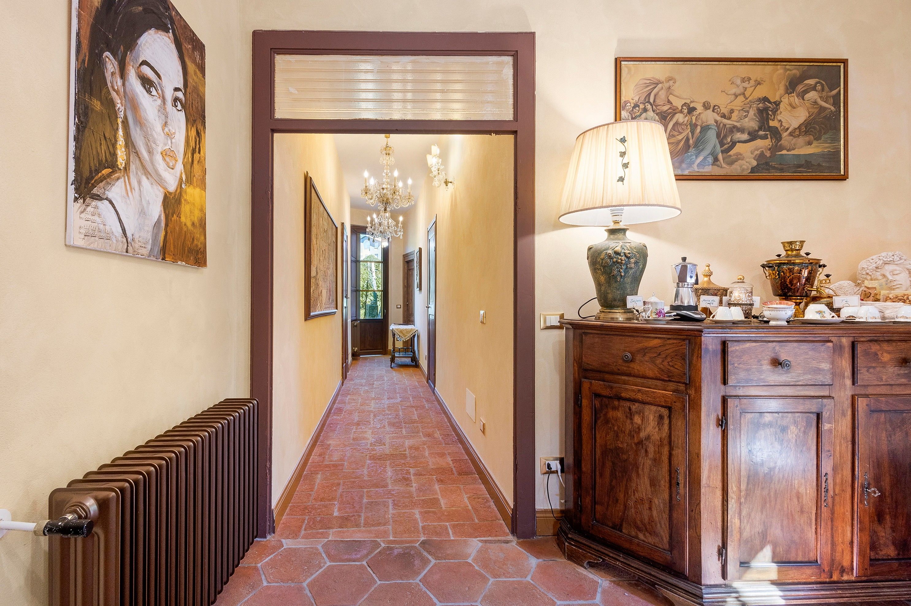 Un couloir avec un radiateur, une armoire en bois sur laquelle est posée une lampe, et un tableau accroché au mur.
