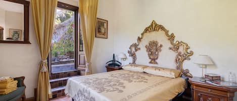 A hotel room with a large bed, a nightstand, a dresser, a window with curtains, and a chandelier.