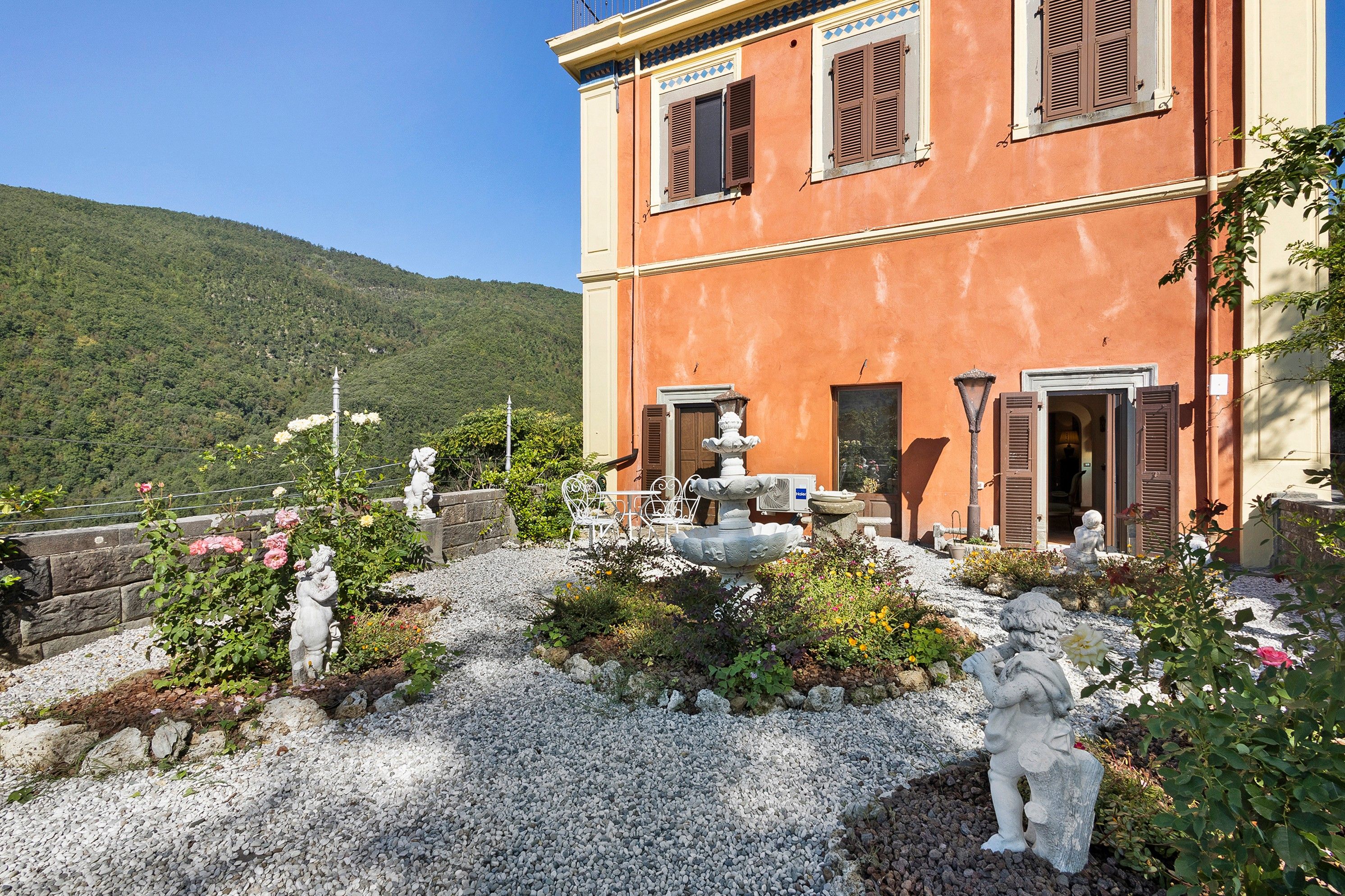 Un edificio con un giardino che presenta statue, una fontana e vista su una collina boscosa.