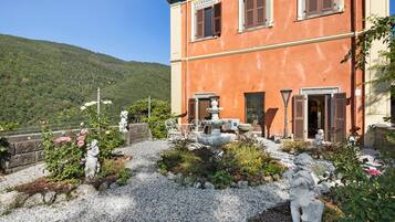 Un edificio con un giardino che presenta statue, una fontana e vista su una collina boscosa.