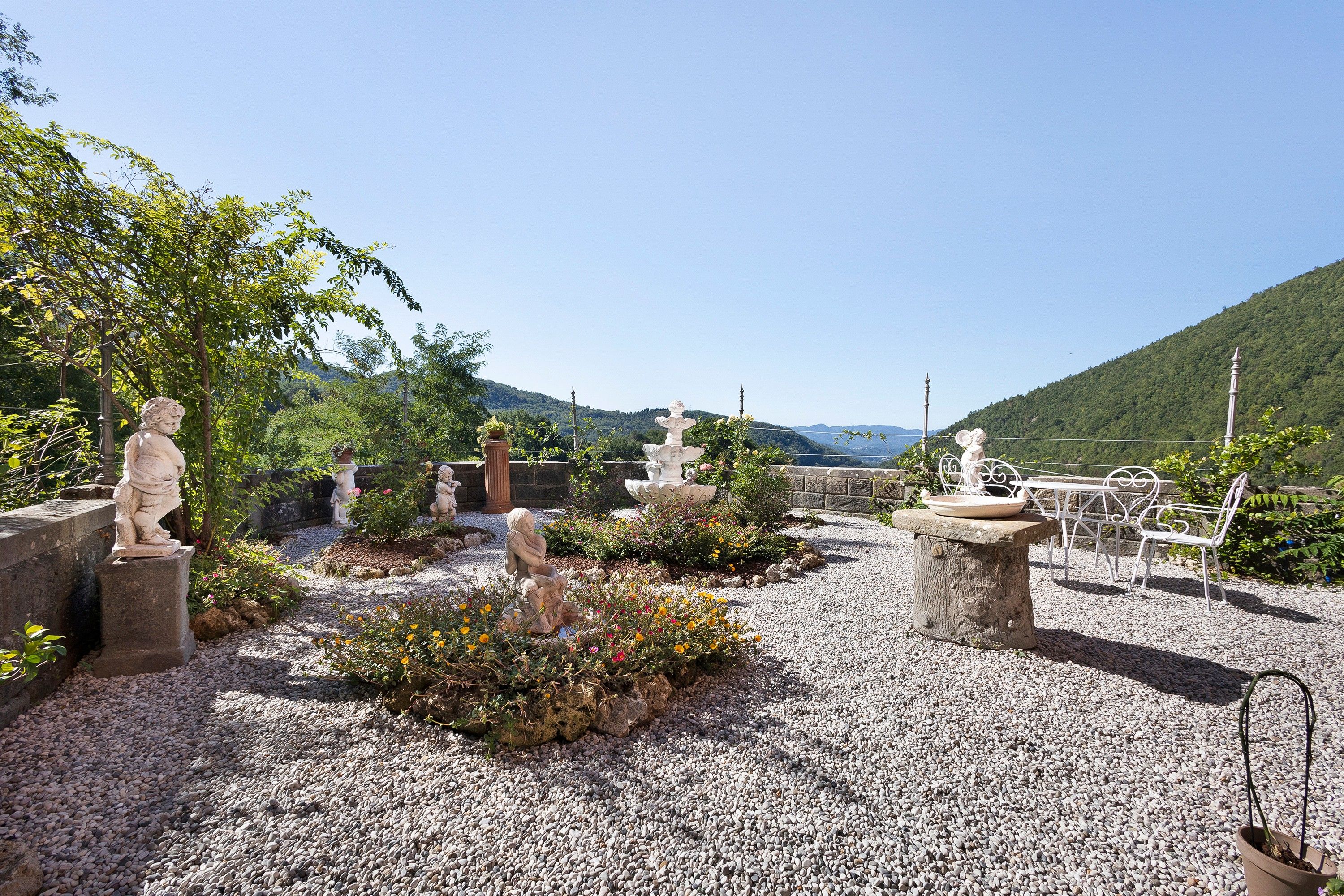 Un jardin agrémenté de statues, d’un banc et offrant une vue sur une montagne.