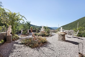 Ein Garten mit Statuen, einer Bank und Blick auf einen Berg.