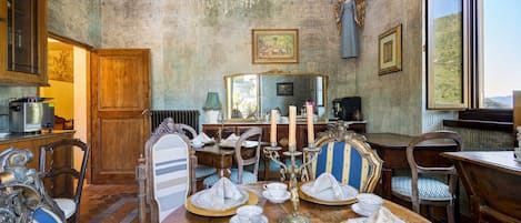 Uma sala de jantar com um candelabro, papel de parede ornamentado e vista pela janela.