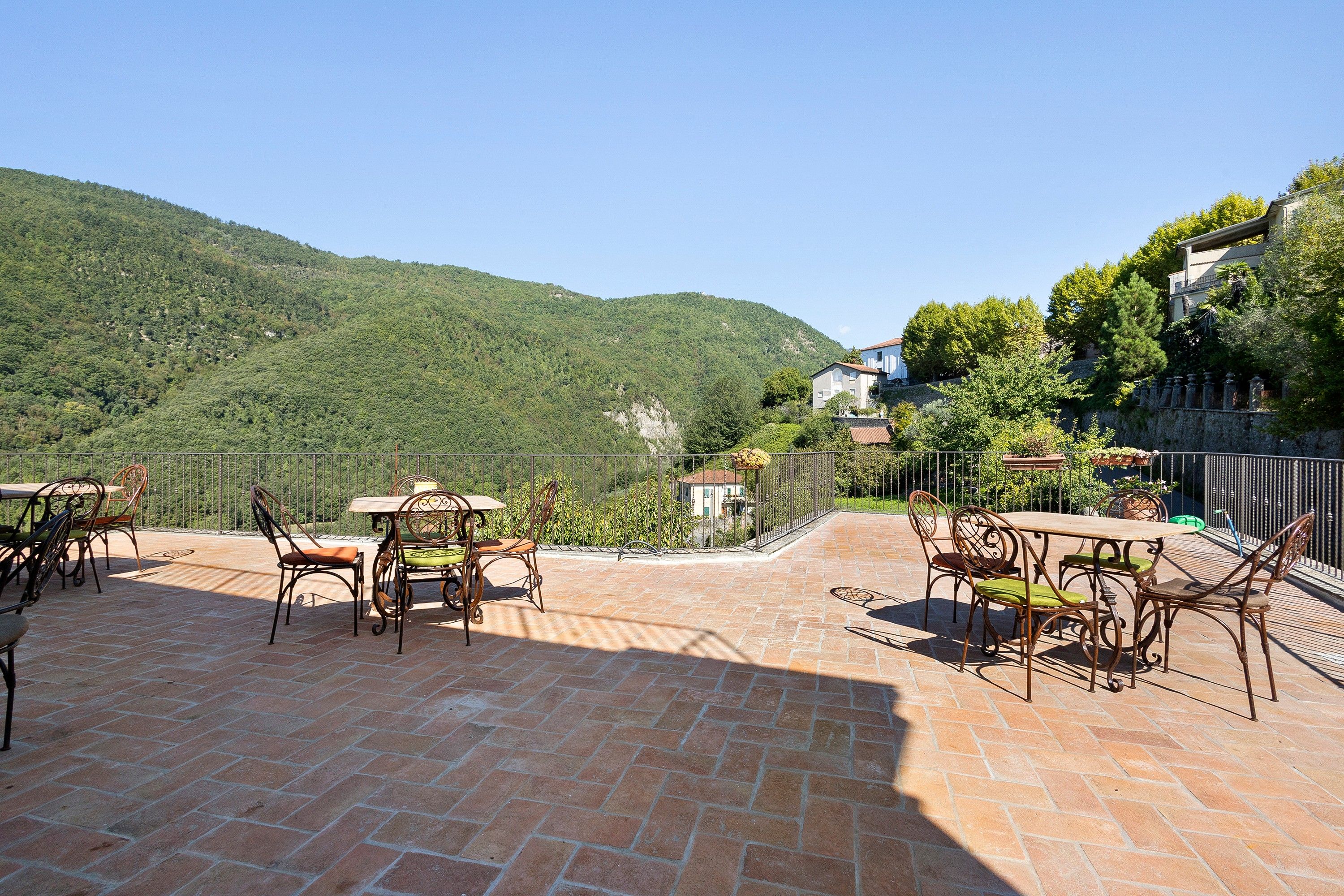An outdoor patio with brick flooring and metal furniture, overlooking a hillside.