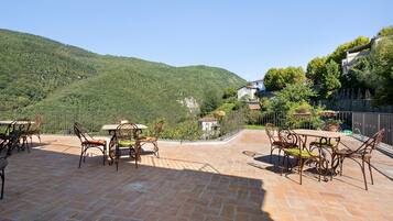 Patio esterno con pavimento in mattoni e mobili in metallo, affacciato su una collina.