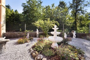 Ein Garten mit einer zentralen Fontäne, umgeben von Kies und unterschiedlichen Pflanzen.