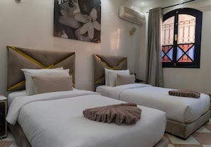 A hotel room with two beds, a large window with a view, an air conditioning unit, and a painting on the wall. - Riad Douirtna (Marrakech)