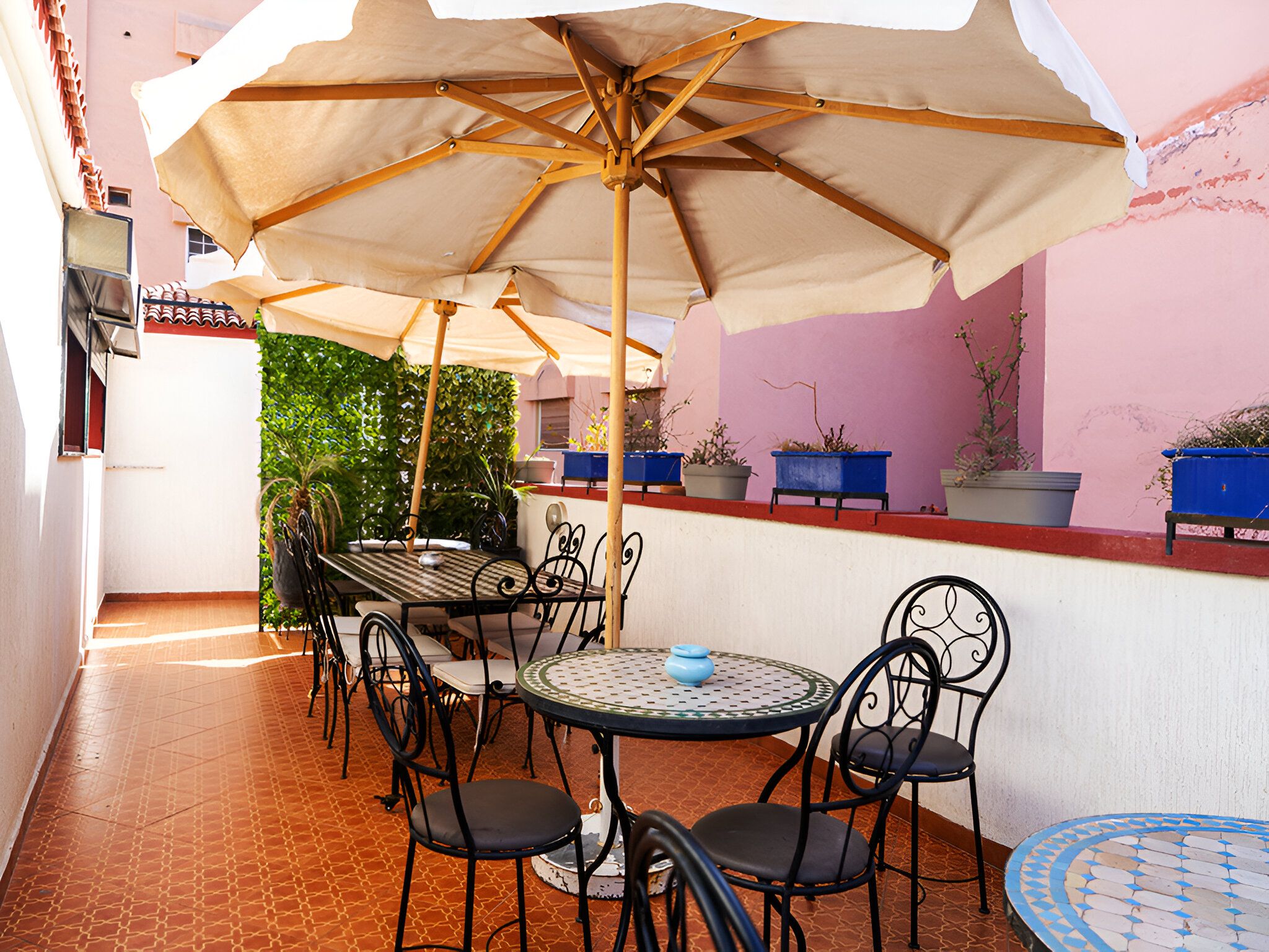 Un patio al aire libre con una mesa, sillas, un paraguas grande y plantas en macetas.