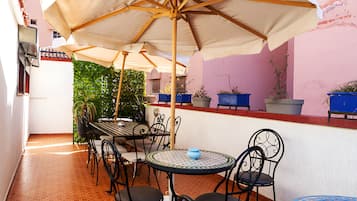 Un patio al aire libre con una mesa, sillas, un paraguas grande y plantas en macetas.
