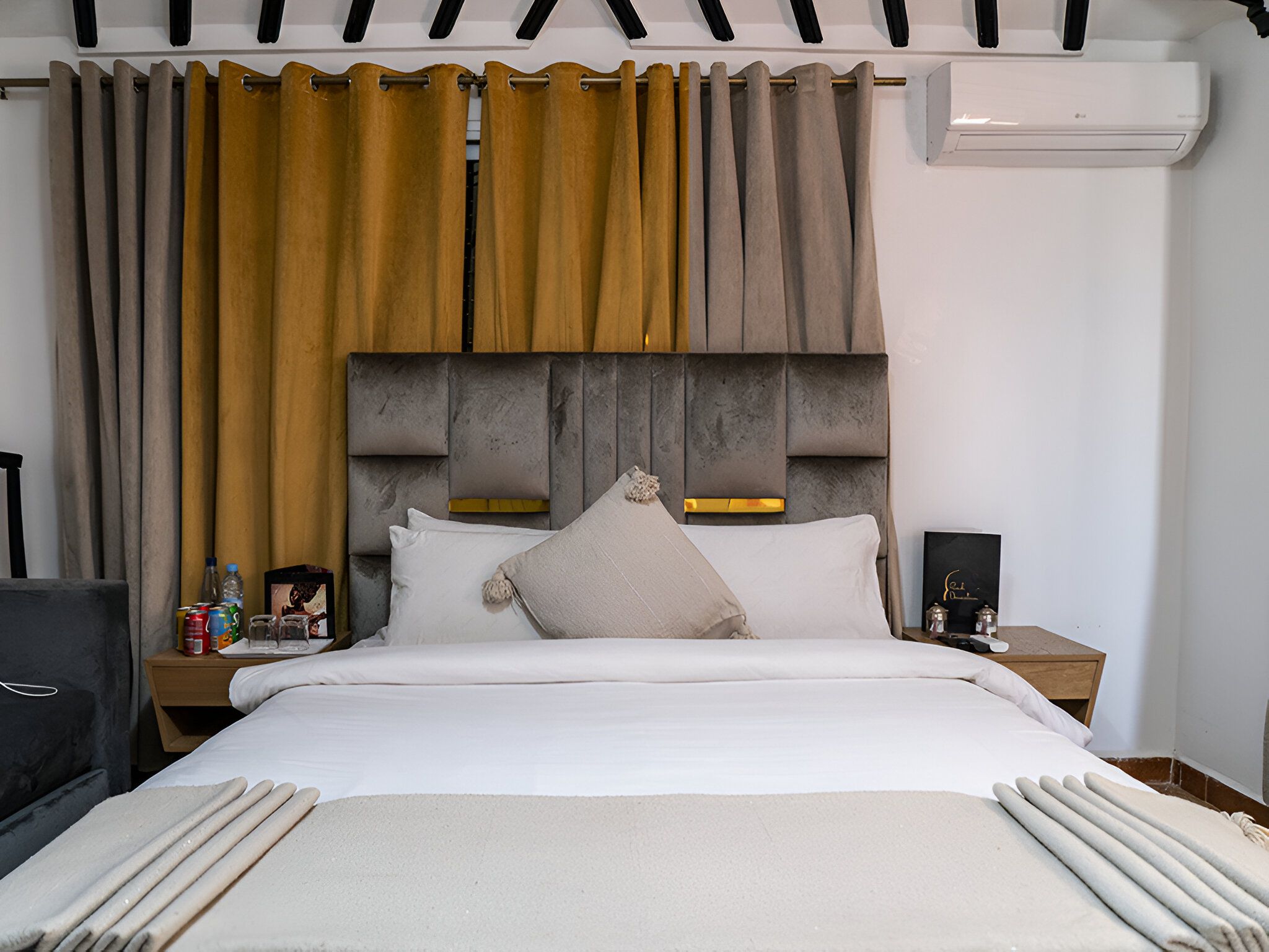 Una habitación de hotel con cama, mesita de noche, lámpara y aire acondicionado instalado en la pared.