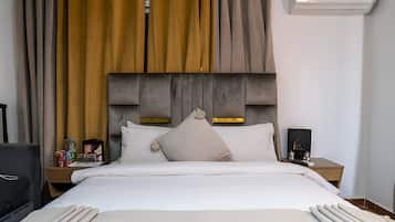 Una habitación de hotel con cama, mesita de noche, lámpara y aire acondicionado instalado en la pared.