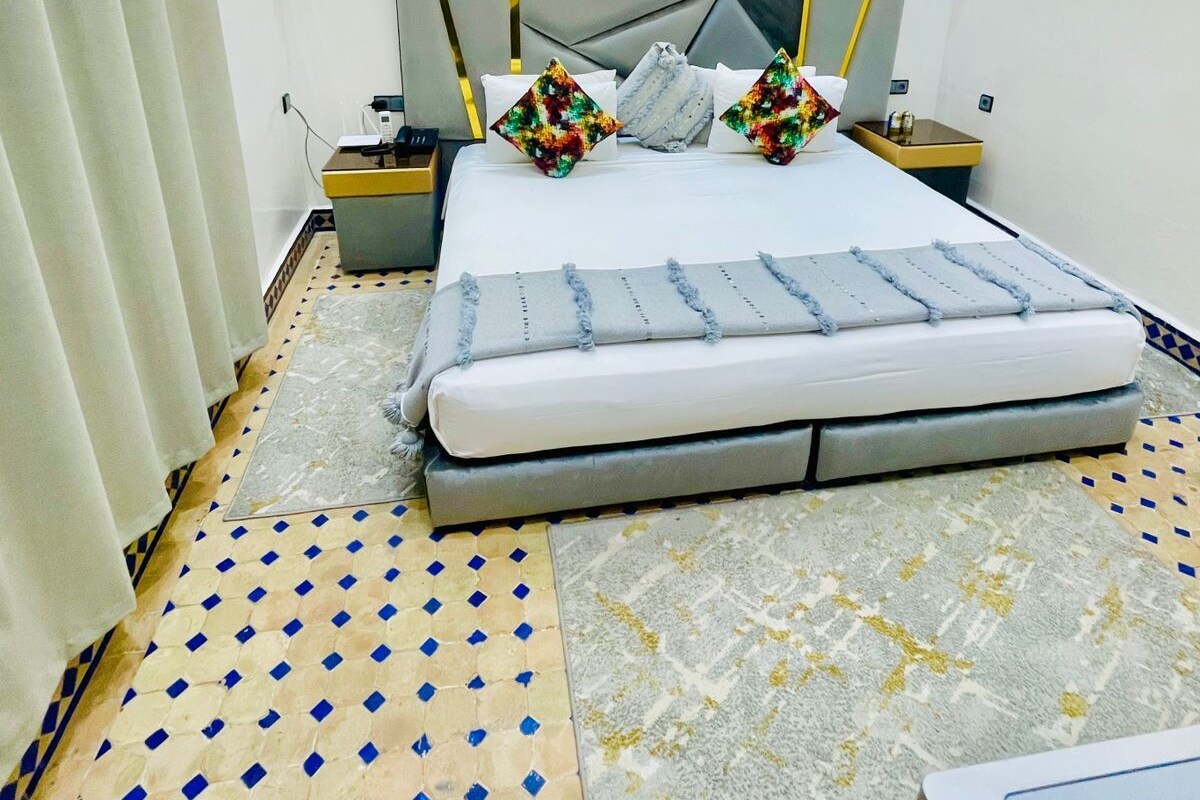Un dormitorio moderno con una cama grande, almohadillas decorativas, cabecera, mesitas de noche y una obra de arte colgada en la pared.